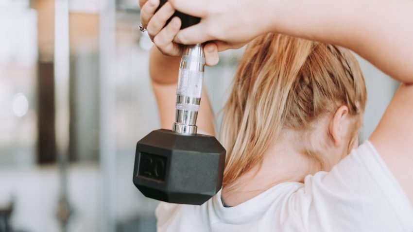 woman holding dumbbell in white crew-neck t-shirt